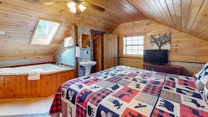 Une cabane confortable avec un intérieur en bois, un grand lit avec une courtepointe, une baignoire, un ventilateur de plafond, un lavabo et un téléviseur.