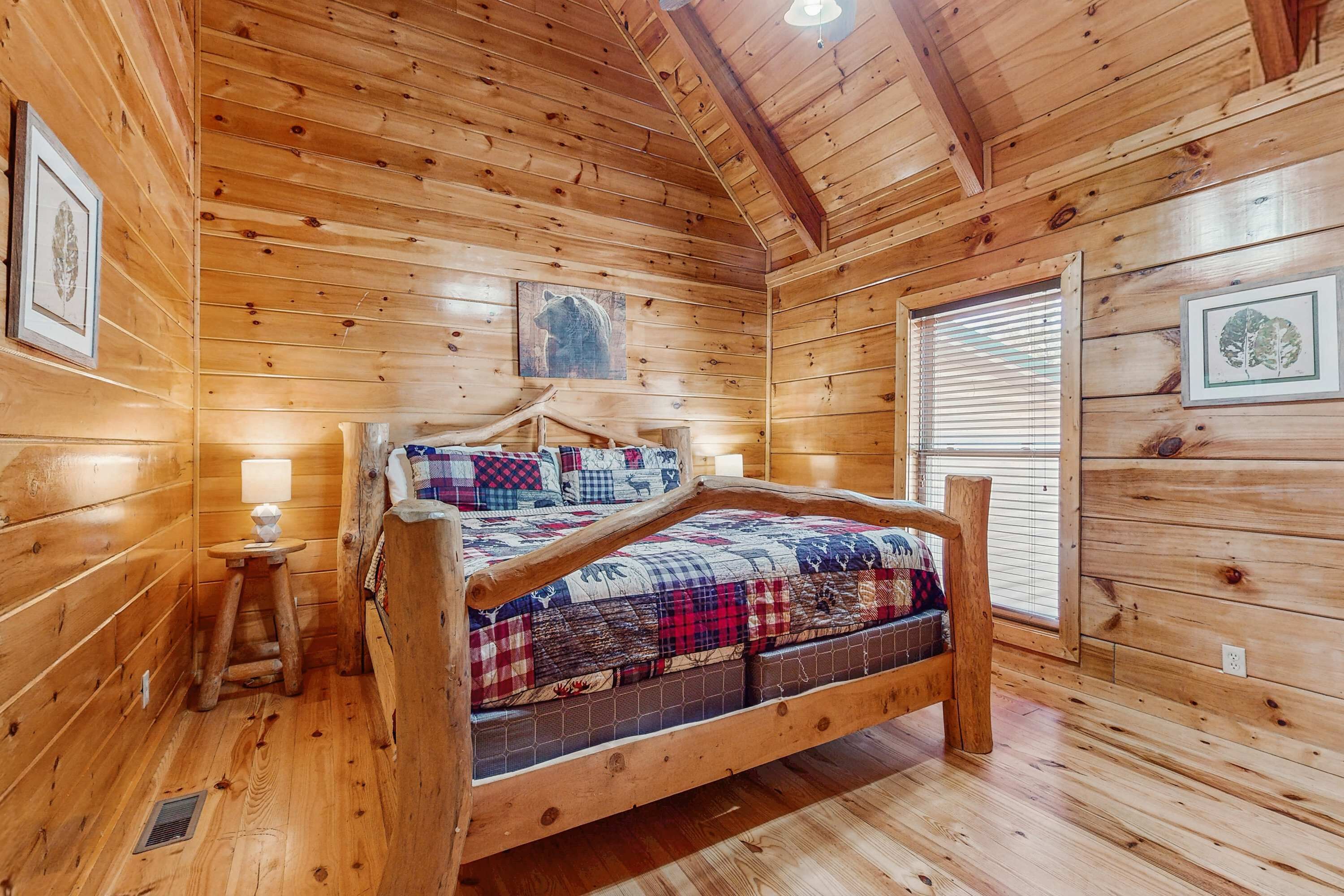 Un dormitorio de cabaña de madera con una cama, una mesita con una lámpara y cuadros en las paredes.