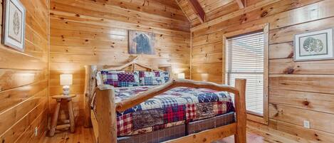 Un dormitorio de cabaña de madera con una cama, una mesita con una lámpara y cuadros en las paredes.
