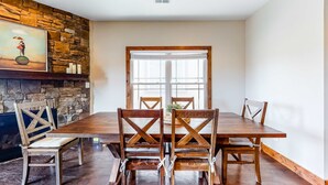 Un comedor con mesa y sillas de madera, pared de piedra y una ventana grande.
