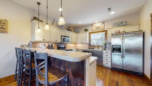 A kitchen with wooden flooring, white cabinets, stainless steel appliances, and a bar area with stools. - Spacious Norris Lake Retreat・View・Deck・BBQ Grill (Andersonville)