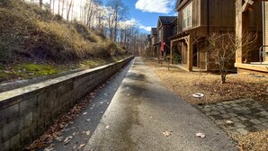 A pathway flanked by wooden buildings with a stone wall on one side and a grassy slope on the other. - Spacious Norris Lake Retreat・View・Deck・BBQ Grill (Andersonville)