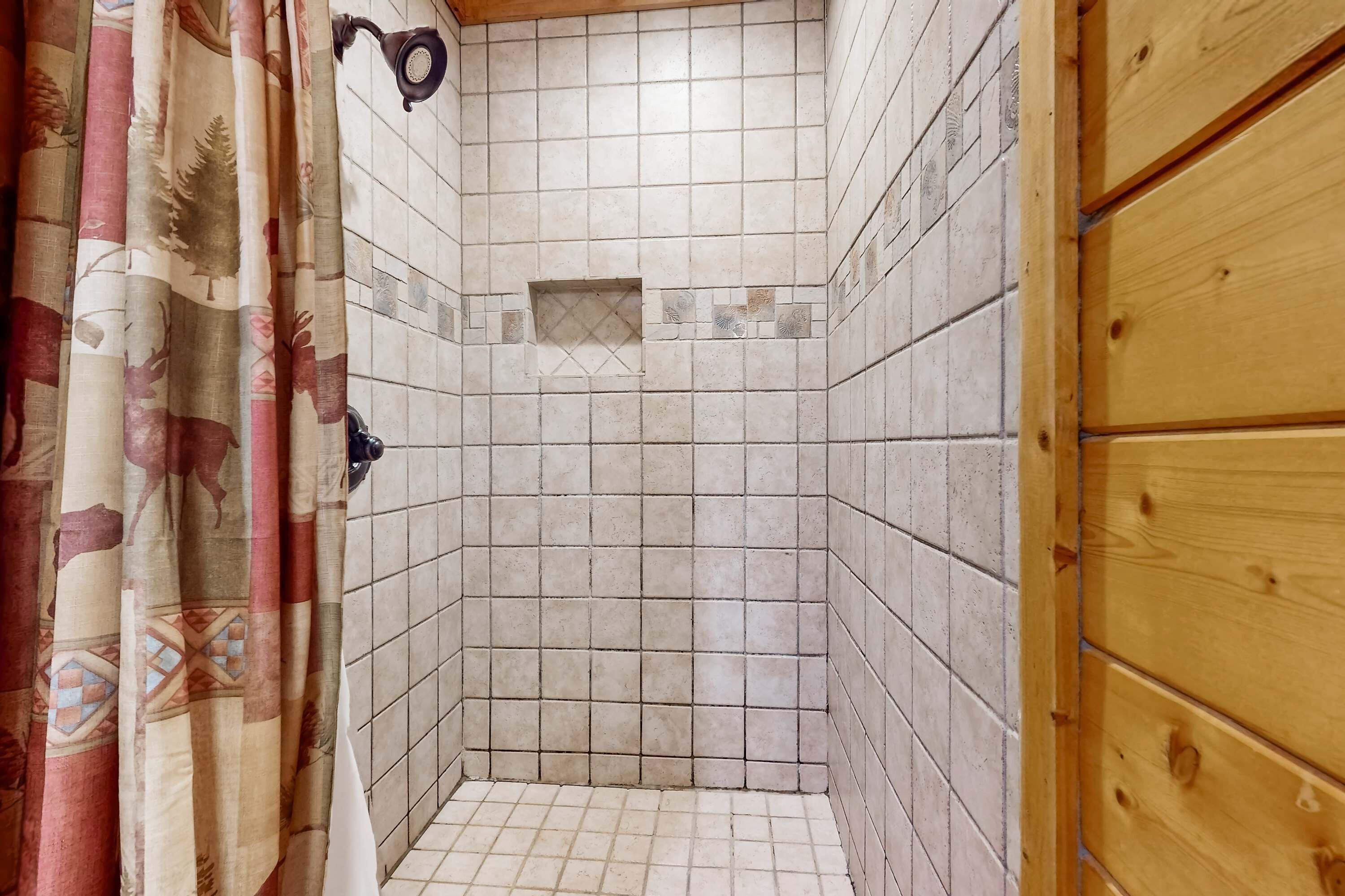 Un angolo doccia piastrellato con una porta in legno e una tenda decorata con un motivo a cervo.