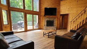 A spacious living room with a stone fireplace, wooden walls, a leather sofa, and a television mounted above the fireplace. - 13.7 Mi to DT  Gatlinburg・Spacious Cabin・Hot Tub (Gatlinburg)