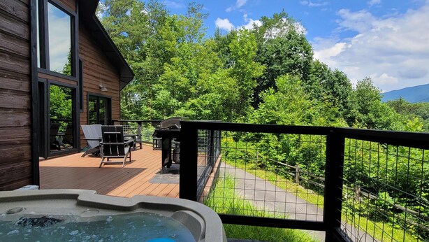 A wooden deck with a hot tub, outdoor furniture, and a view of a forested area. - 13.7 Mi to DT  Gatlinburg・Spacious Cabin・Hot Tub (Gatlinburg)