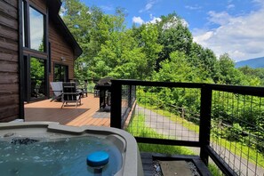 Una terraza de madera con un jacuzzi, mobiliario exterior y vistas a un área boscosa.
