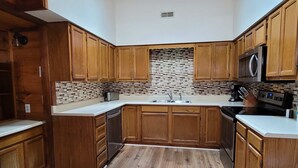 A kitchen with wooden cabinets, a tiled backsplash, a stainless steel microwave, and a dishwasher. - 13.7 Mi to DT  Gatlinburg・Spacious Cabin・Hot Tub (Gatlinburg)