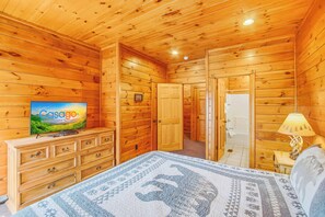 Ein Zimmer in einer Holzhütte mit Bett, Kommode, Fernseher und Lampe.