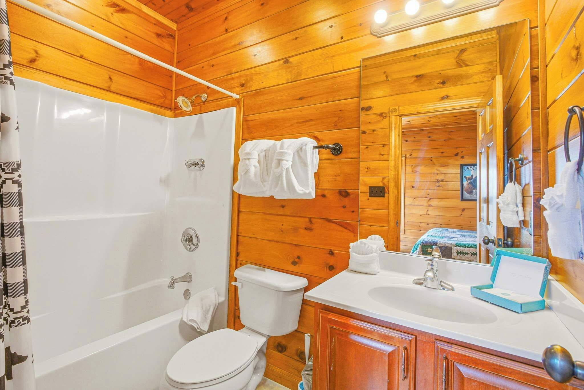 Une salle de bain rustique, aménagée dans une cabane en bois, avec une baignoire, des toilettes, un lavabo et un grand miroir.