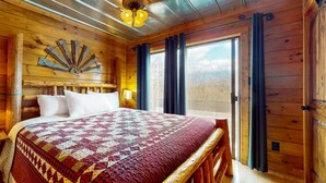 Ein Schlafzimmer einer Holzhütte mit einem großen Bett, einem Deckenventilator und Blick ins Freie durch ein Fenster.