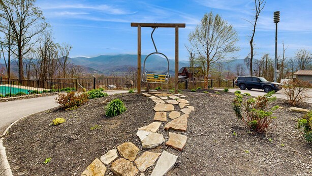 Ein Steinweg führt zu einer Holnpergola mit einer Hängematte, umgeben von angelegten Gärten und einer Bergblick.