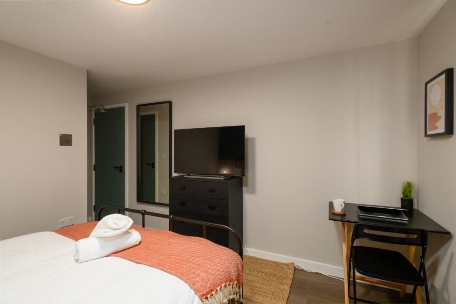 A hotel room with a bed, a desk with a chair, a television, and a mirror.