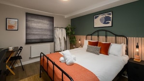 A neatly arranged bedroom with a bed, bedside table, and a desk with a chair. - Benjamin Suite Modern 3BR Apartment (Cardiff)