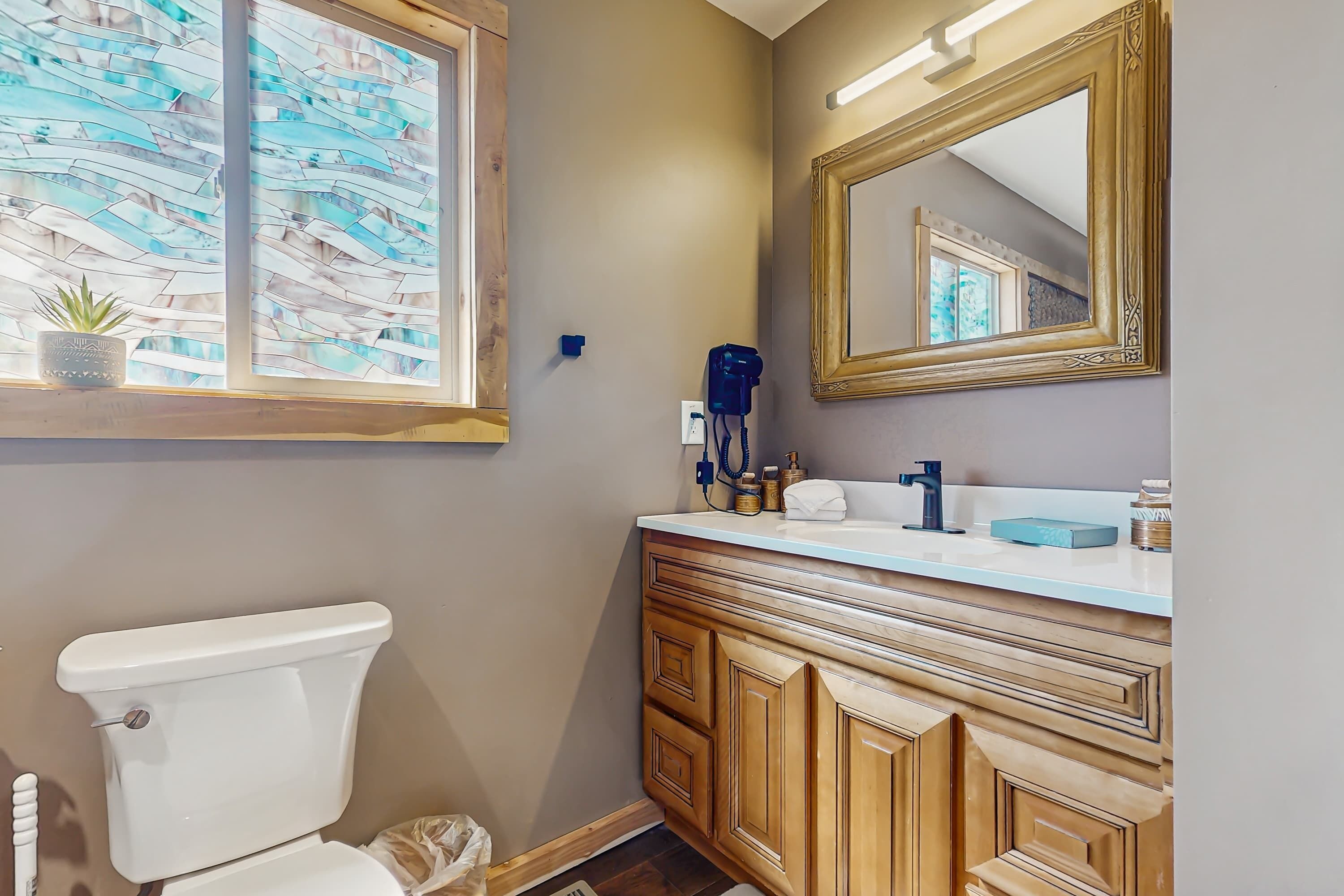 A bathroom with a toilet, vanity, mirror, and window with a view of the outside.