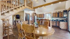A spacious dining area with a wooden staircase, a large wooden dining table, and matching chairs. - Cozy Lake Front Cabin, Sleeps 4, Dock, Play Yard (Dandridge)