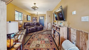 A living room with a brown leather sofa, a patterned rug, a wooden cabinet, and a flat-screen TV mounted on the wall. - Cozy Lake Front Cabin, Sleeps 4, Dock, Play Yard (Dandridge)