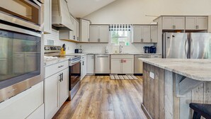 Una cocina moderna con electrodomésticos de acero inoxidable, armarios blancos y piso de madera.
