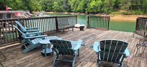 Eine Holzterrasse mit Adirondack-Stühlen und einem Tisch, mit Blick auf ruhiges Wasser, umgeben von Bäumen.