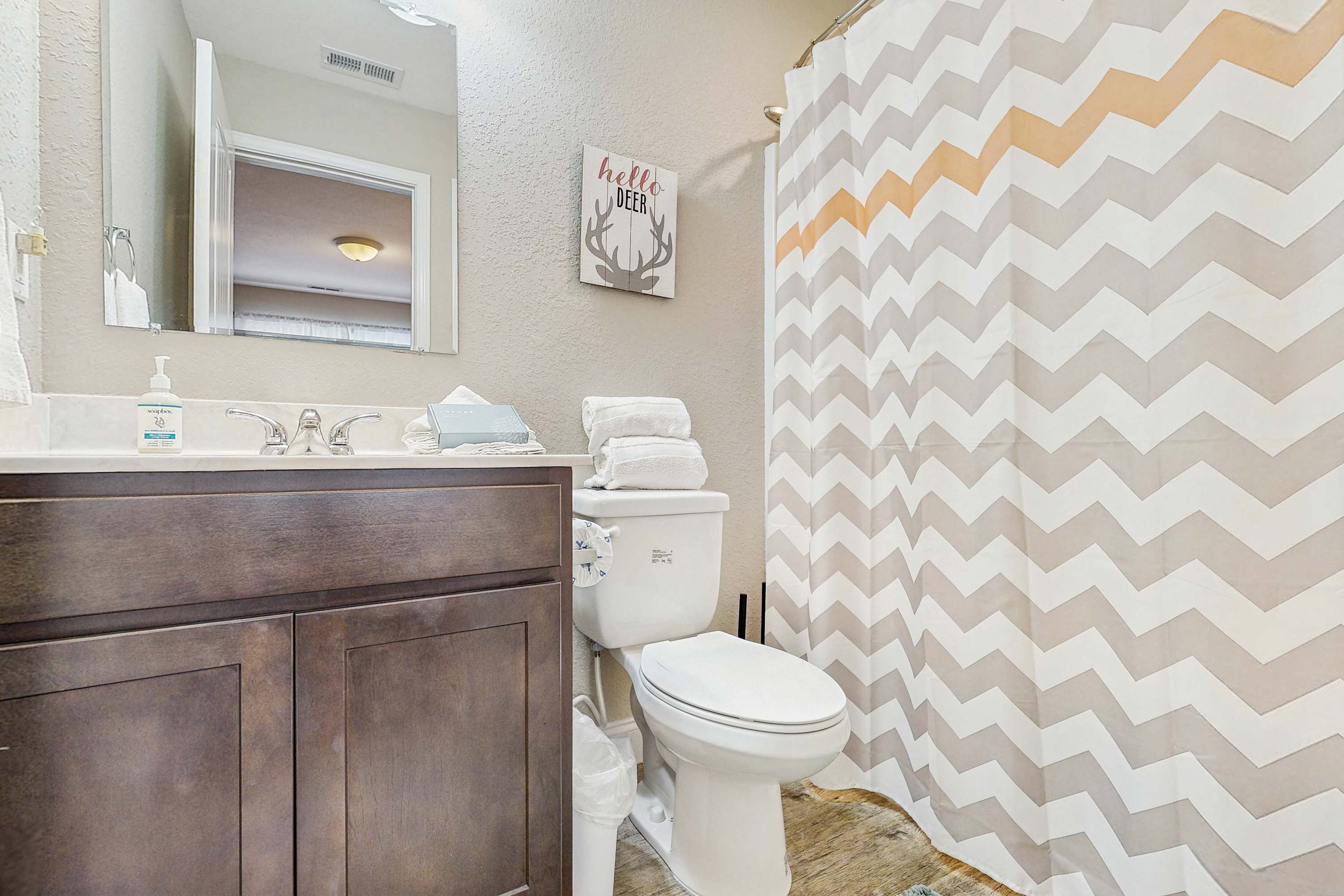 A bathroom with a wooden vanity, a white toilet, a mirror, and a shower curtain with a zigzag pattern.