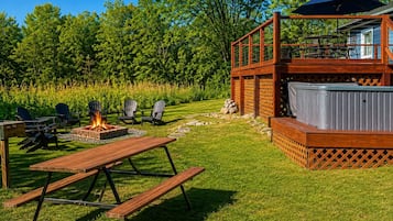 Un patio al aire libre con una chimenea, mesa de picnic, sillas Adirondack y un jacuzzi.