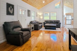 Ein geräumiges Wohnzimmer mit Holzboden, zwei Ledersofas, einem Couchtisch und einem Kamin.