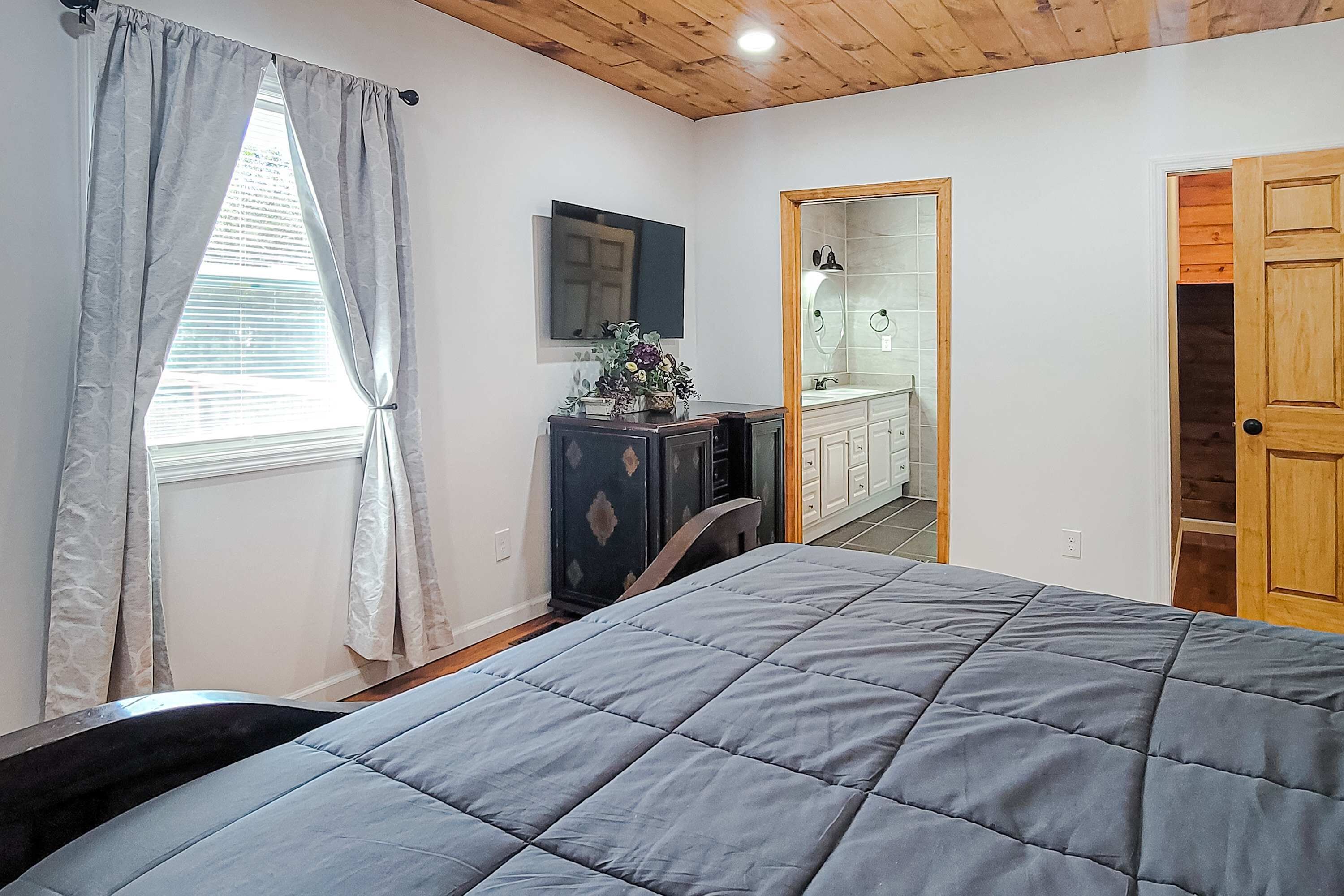 Un dormitorio con cama, cómoda, espejo y ventana con cortinas.