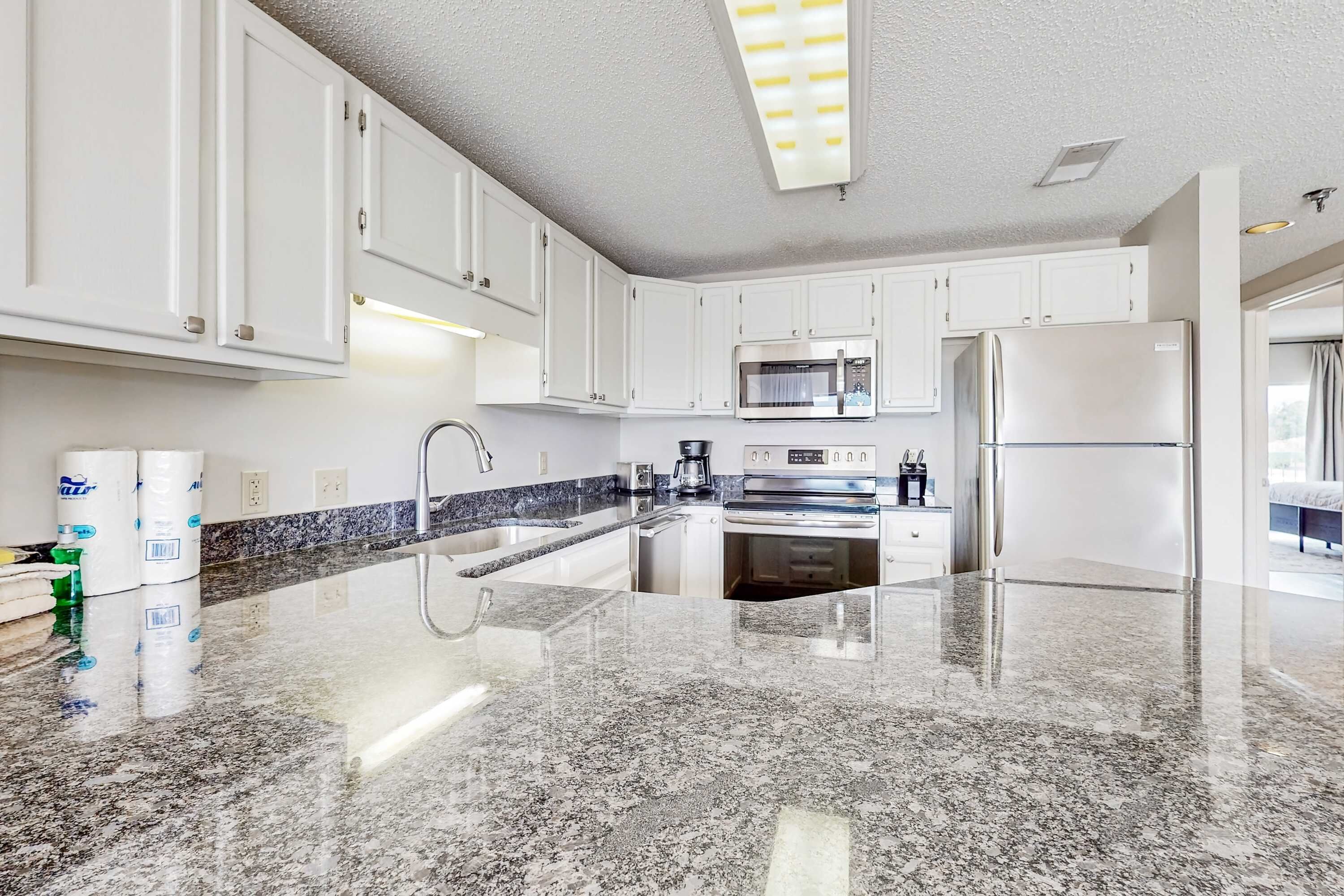 A modern kitchen with white cabinets, granite countertops, stainless steel appliances, and under-cabinet lighting.
