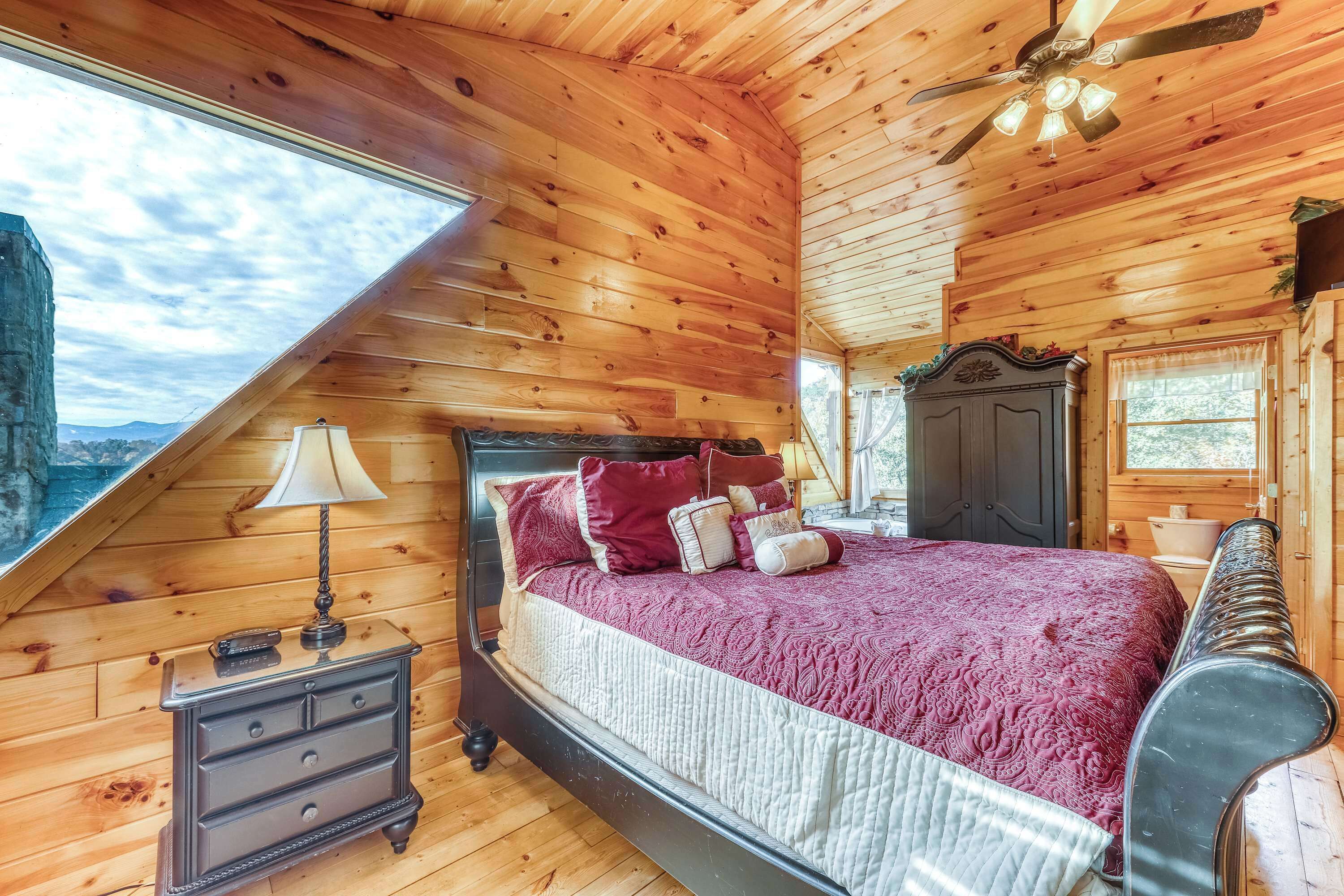 A wooden cabin bedroom with a bed, nightstand, and a ceiling fan.