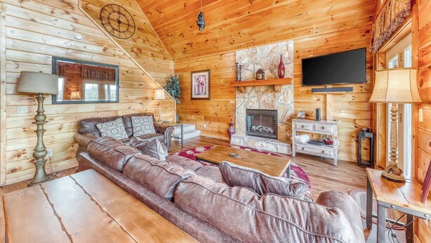 A cozy log cabin interior with a leather sofa, wooden flooring, a fireplace, and a mounted television. - Spacious, Dog Welcome Cabin, Sleeps 8・Mtn Views (Pigeon Forge)