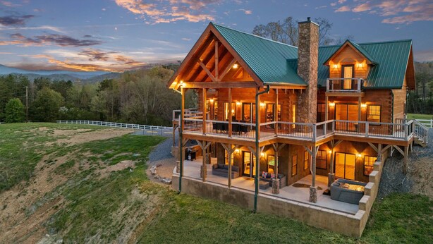 A large log cabin with multiple decks and a stone chimney, surrounded by a fenced property. - Spacious Cabin, Sleep 22, Hot Tub, Game, Theatre, View (Pigeon Forge)