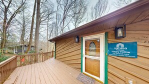 Eine Holzhütte mit Holzterrasse, Fußmatte und einem Schild für Vacasa Tennessee Happy Hollow.