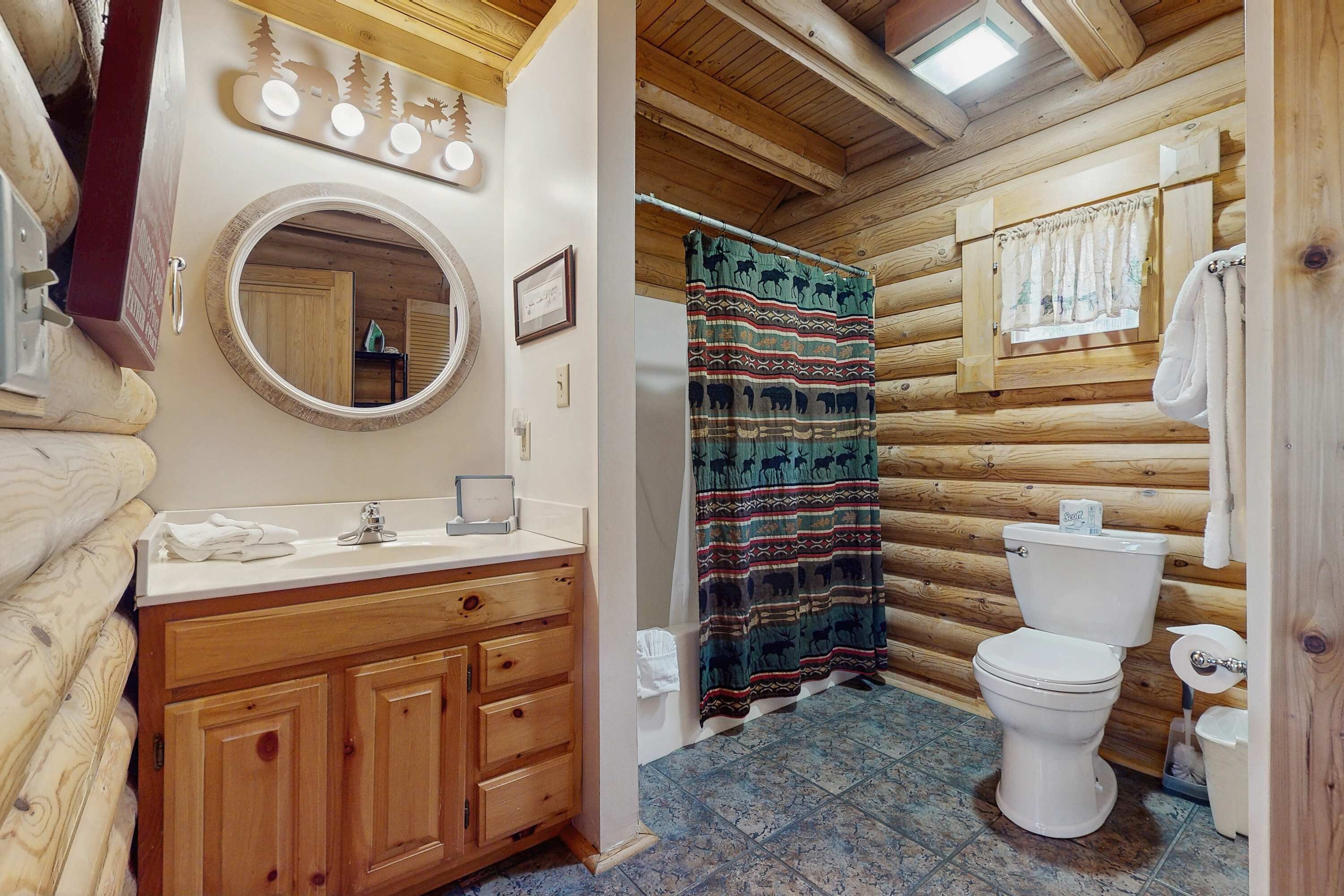 Bagno di una baita in legno con un mobile bagno in legno, un water e una tenda da doccia.