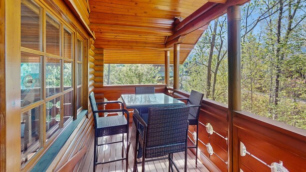 A wooden deck with a glass table and chairs, surrounded by large windows offering a view of trees. - Quiet Gatlinburg Retreat・Hot tub・Fireplace・Pool (Gatlinburg)