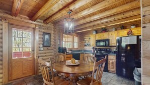 A wooden cabin interior with a dining table surrounded by chairs, a kitchen area with appliances, and a large window. - Quiet Gatlinburg Retreat・Hot tub・Fireplace・Pool (Gatlinburg)