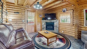 A log cabin interior with a leather sofa, a wooden coffee table, a fireplace, a television, and a sign indicating a cabin and hiking trails. - Quiet Gatlinburg Retreat・Hot tub・Fireplace・Pool (Gatlinburg)
