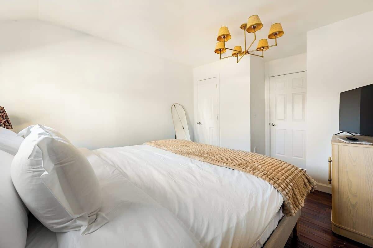 A bedroom with a bed, a wooden dresser, a television, and a ceiling light fixture.