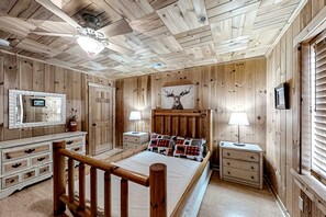 Een slaapkamer met houten lambrisering, een bed, nachtkastjes, een spiegel en een plafondventilator.