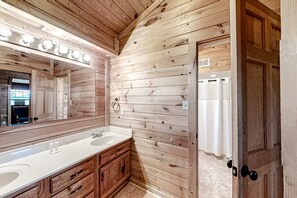Een houten badkamer met een badkamerkastje met twee wasbakken, een grote spiegel en een douchegordijn.