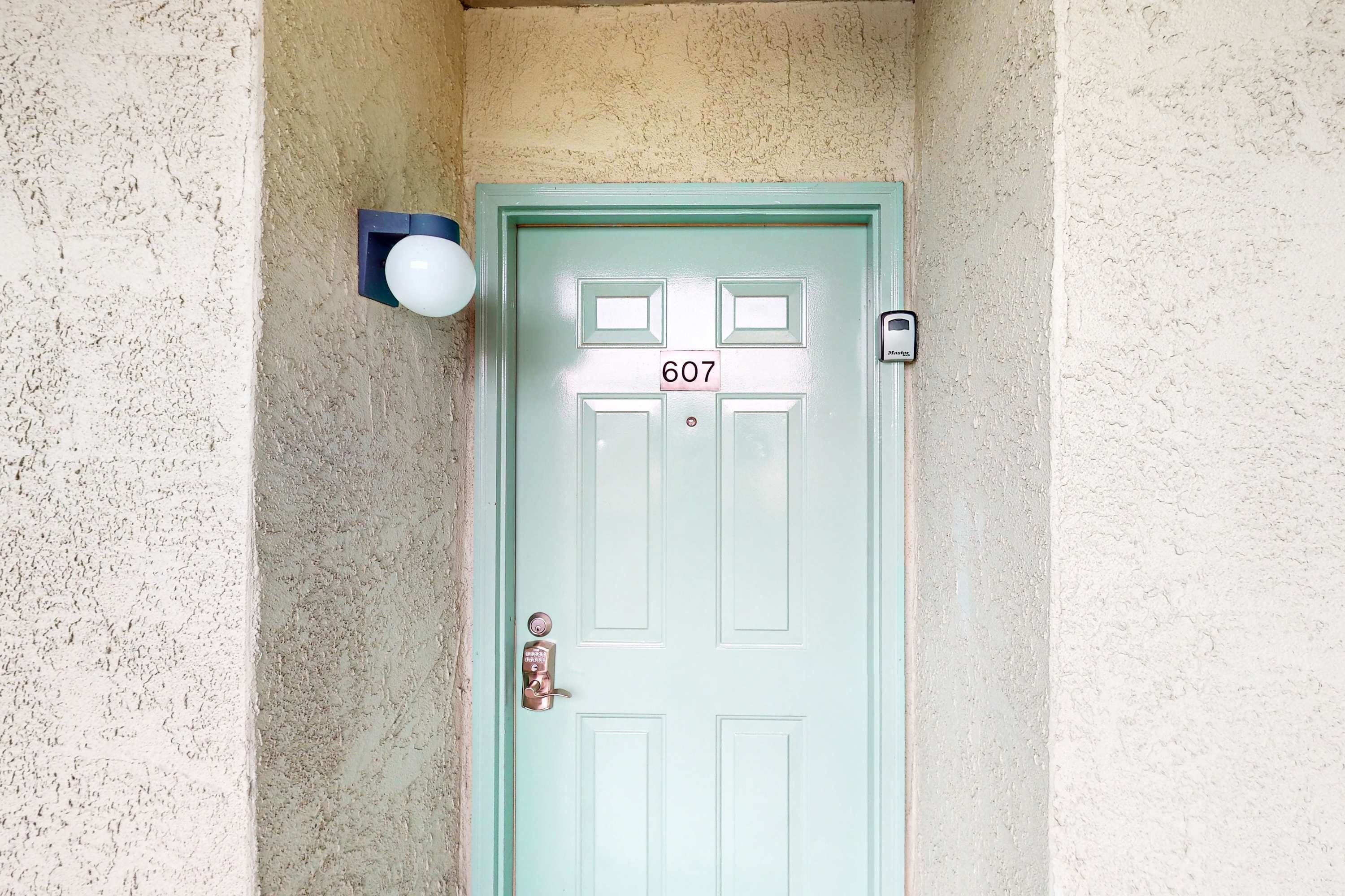 A light green door with the number 607, a wall-mounted light, and a doorbell.