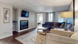 A modern living room with a flat-screen TV, a fireplace, a sofa, and a coffee table. - Dual-Suite Riverside Condo, Sleeps 4, Views, Pool (Pigeon Forge)