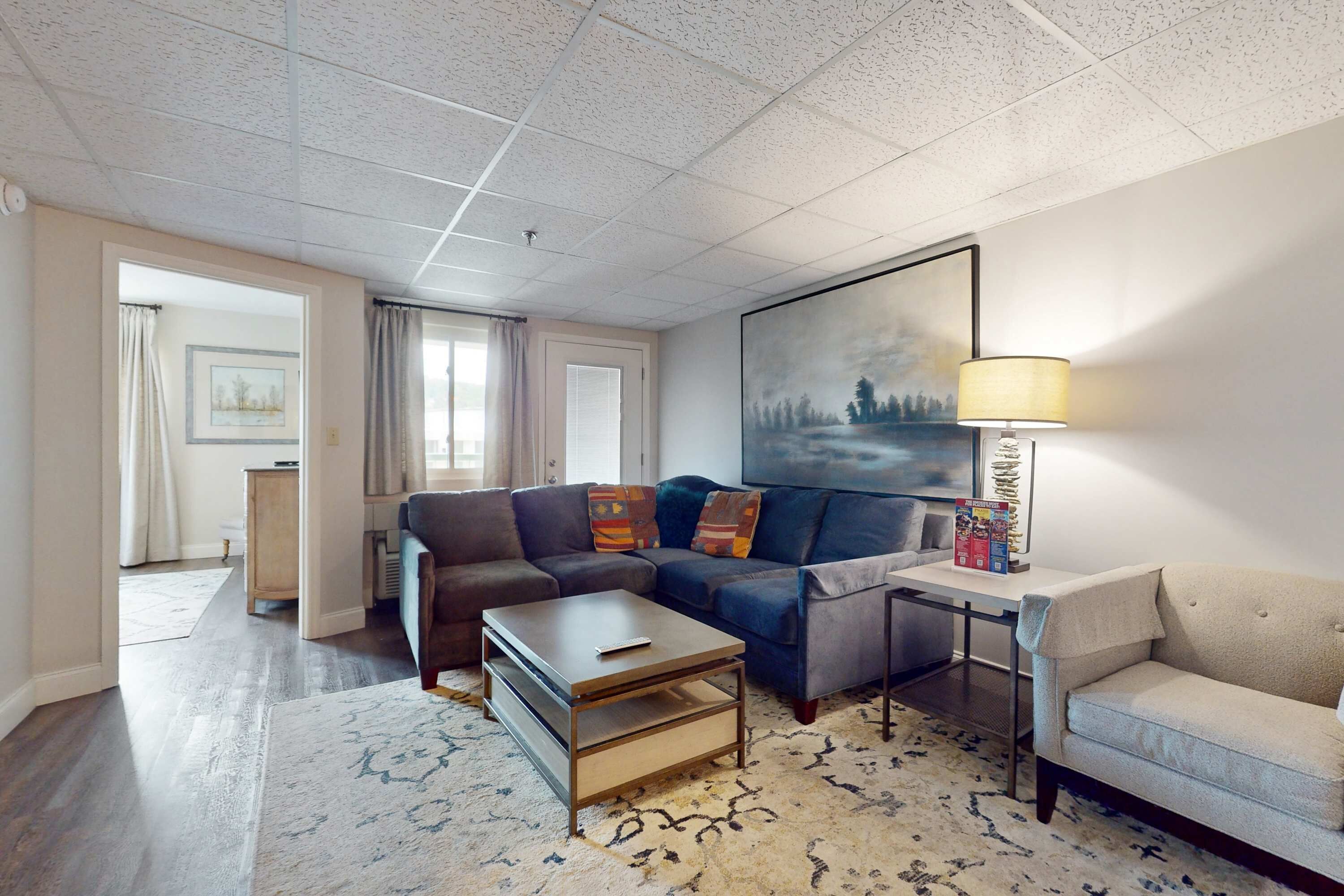 A modern living room with a sectional sofa, a coffee table, a side table with a lamp, and a large painting on the wall.