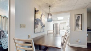 A modern dining area with a wooden table and chairs, a hanging light fixture, and abstract wall art. - Dual-Suite Riverside Condo, Sleeps 4, Views, Pool (Pigeon Forge)