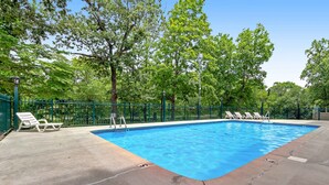 A rectangular swimming pool with a green fence and lounge chairs. - Cozy Riverfront Downtown Condo, Sleeps 6, Balcony (Pigeon Forge)