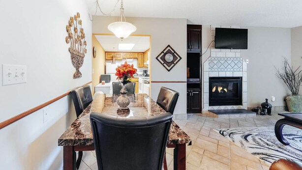 A dining area with a marble table, black chairs, and a vase of flowers. There is a fireplace with a TV mounted above it. - Cozy Riverfront Downtown Condo, Sleeps 6, Balcony (Pigeon Forge)