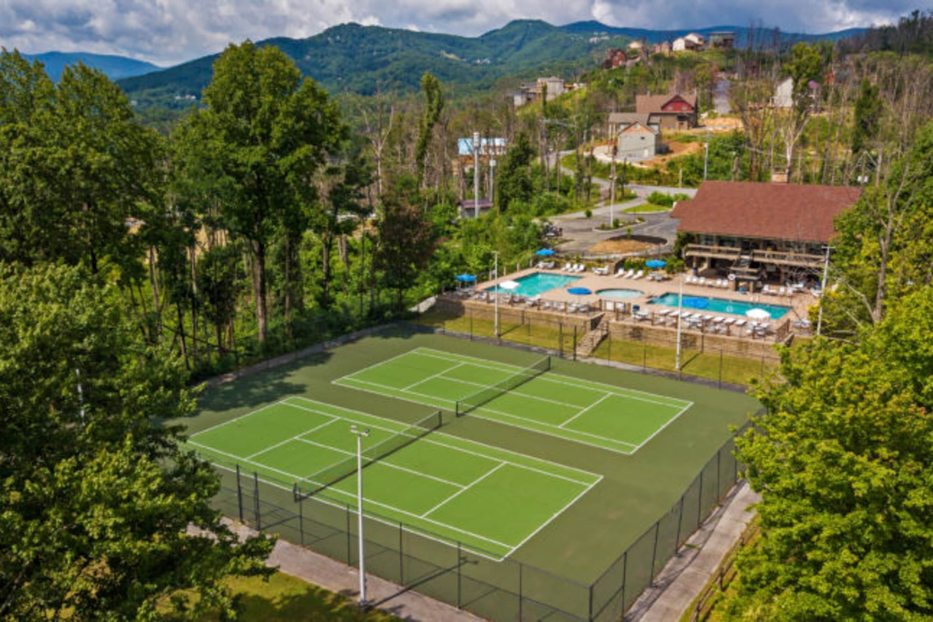 Een tennisbaan omgeven door weelderige begroeiing en een zwembadgedeelte met ligbedden.