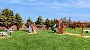 A playground with a slide, swings, and picnic tables in a grassy area with trees in the background. - Mtn View Getaway, Sleeps 6, Bunk nook, Shared Pool (Pigeon Forge)