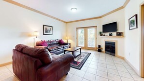 A living room with a brown leather sofa, a coffee table, a fireplace, and a television mounted on the wall. - Mtn View Getaway, Sleeps 6, Bunk nook, Shared Pool (Pigeon Forge)