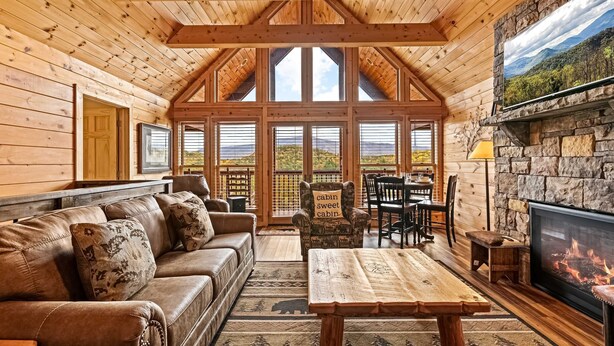 A cozy cabin interior with a wooden ceiling, a fireplace, a sofa, and a dining area. - Cabin Views, Sleeps 12・Foosball・Theater・Putt-putt (Sevierville)