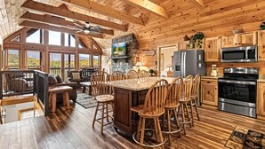 A spacious kitchen with wooden cabinets, a granite island, and a stone fireplace. - Cabin Views, Sleeps 12・Foosball・Theater・Putt-putt (Sevierville)