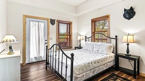 A bedroom with a bed, two nightstands, a lamp, a door, and a window with shutters. - Cabin Views, Sleeps 12・Foosball・Theater・Putt-putt (Sevierville)